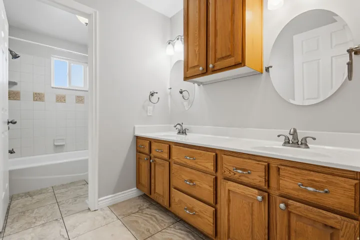 Double vanity with wood-finish cabinetry, white countertops, and dual circular mirrors