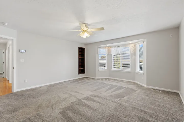 Recessed bay window, built-in shelving, ceiling fan, and light-toned carpeting