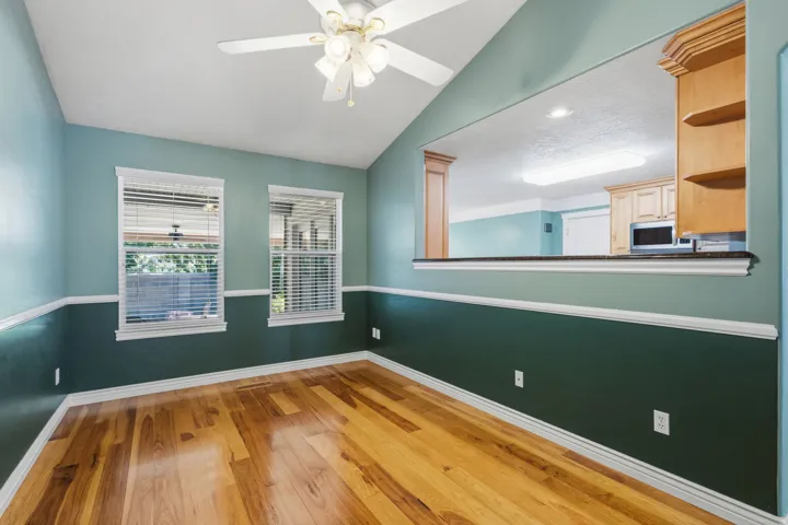 Vaulted ceiling with ceiling fan, wood-finish flooring, two windows with blinds, a pass-through opening with a countertop, and built-in cabinetry