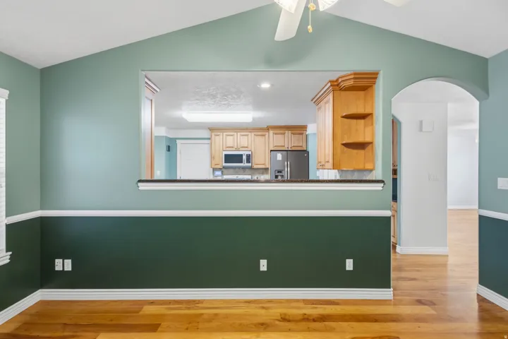 Vaulted ceiling, open pass-through, wood-finish flooring, architectural archway, and ceiling fan with lighting