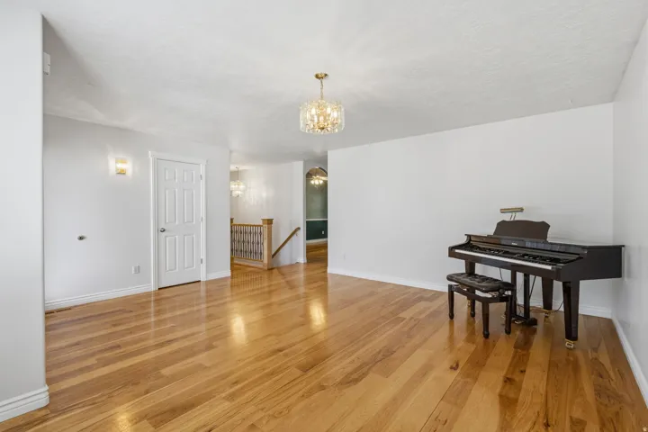 Hardwood flooring, crystal chandelier, wall sconces, white paneled door, and open staircase with wood handrail