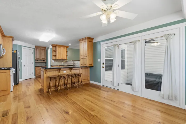 Wood-finish flooring, kitchen island with seating, natural wood cabinetry, pendant lighting, and ceiling fan