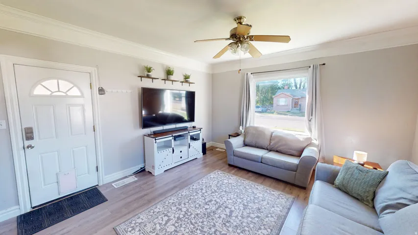 Crown molding, wood-finish flooring, ceiling fan with integrated lighting, large window with natural light, and a paneled entry door