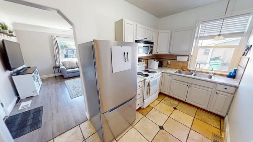 Kitchen with white cabinetry, a double basin sink, tile flooring, and a window
