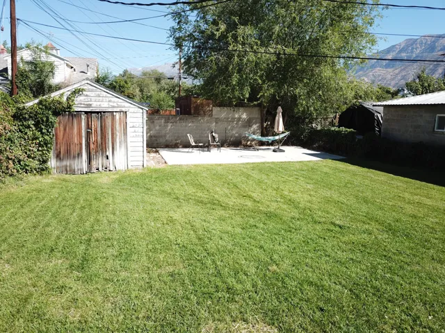 Expansive lawn with a concrete patio, a detached shed, a retaining wall, and mature trees