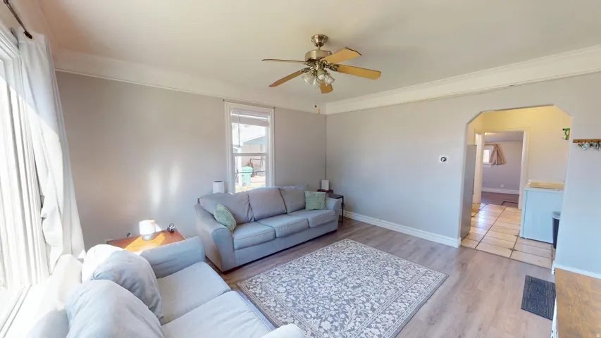 Wood-finish flooring, ceiling fan with light fixture, large windows, and a cased opening