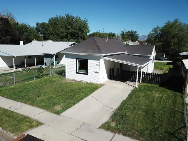 White exterior siding with dark trim windows, dark shingle roof, covered entry, and a paved driveway