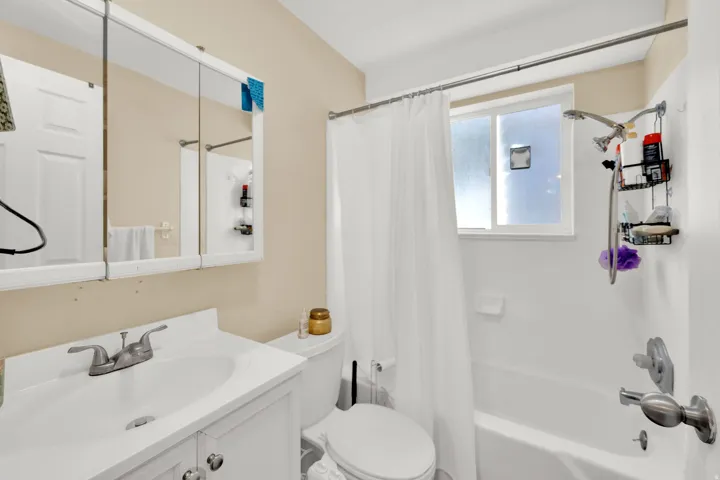 White vanity with cabinet storage, chrome faucet, white medicine cabinet, and white shower-over-tub combination