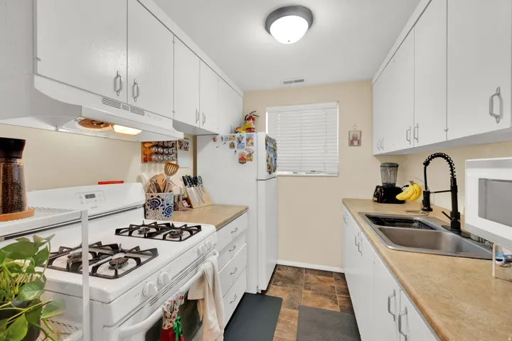 White cabinetry with brushed nickel hardware, laminate countertops, dual basin stainless steel sink with a black pull-down faucet, and resilient flooring