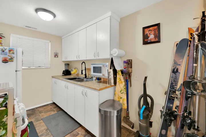 White cabinetry, light countertop, dual basin sink with black faucet, tiled flooring, and window with blinds