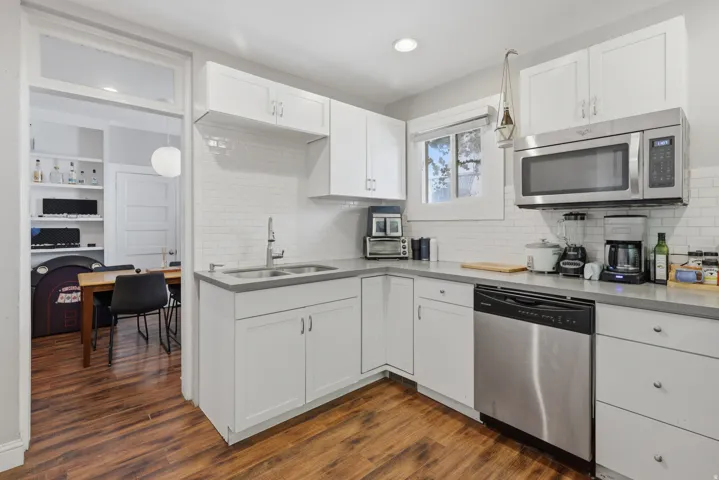 Modern kitchen featuring white shaker cabinetry, stainless steel appliances, a subway tile backsplash, light-toned countertops, and wood-finish flooring