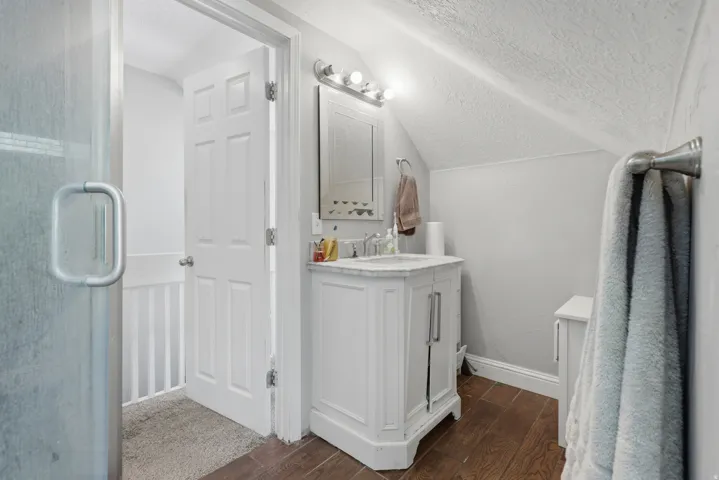 White vanity with integrated sink, dark wood-finish flooring, glass shower enclosure, and sloped ceiling