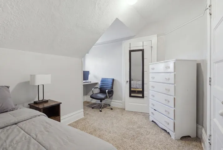 Carpeted flooring, built-in desk, white painted trim, interior door, overhead lighting