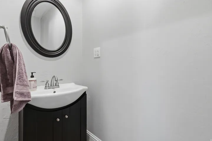 Pedestal sink with a brushed nickel faucet, a dark wood-finish vanity with polished chrome hardware, and an oval mirror with a dark frame