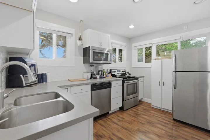 Kitchen featuring wood-finish flooring, white cabinetry, stainless steel appliances, and a double basin sink