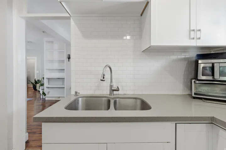 Modern kitchen featuring a double-basin stainless steel sink, gooseneck faucet, light-toned countertop, and white subway tile backsplash