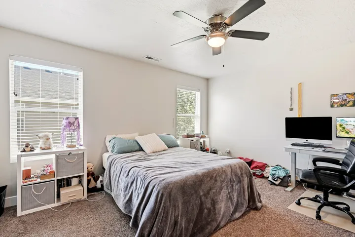 Recessed lighting, ceiling fan with integrated lighting, two windows with horizontal blinds, and carpeted flooring