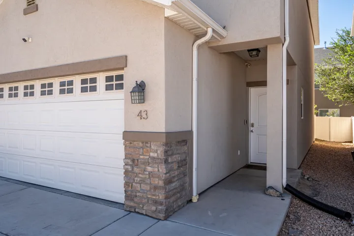 Stucco exterior with stone veneer accents, white panel garage door with window inserts, covered entryway with a white paneled door, exterior sconce lighting, and concrete driveway