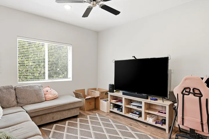 Recessed ceiling lighting, a ceiling fan with integrated lighting, a window with horizontal blinds, wood-finish flooring, and a built-in media console