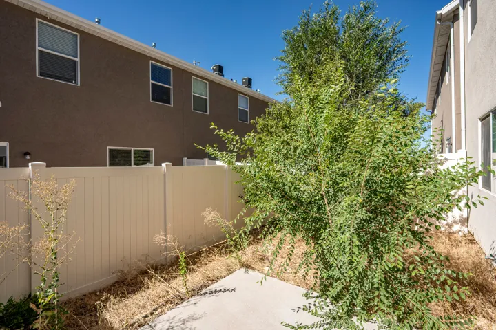 Enclosed outdoor space featuring a concrete pad, mature shrubbery, and a privacy fence