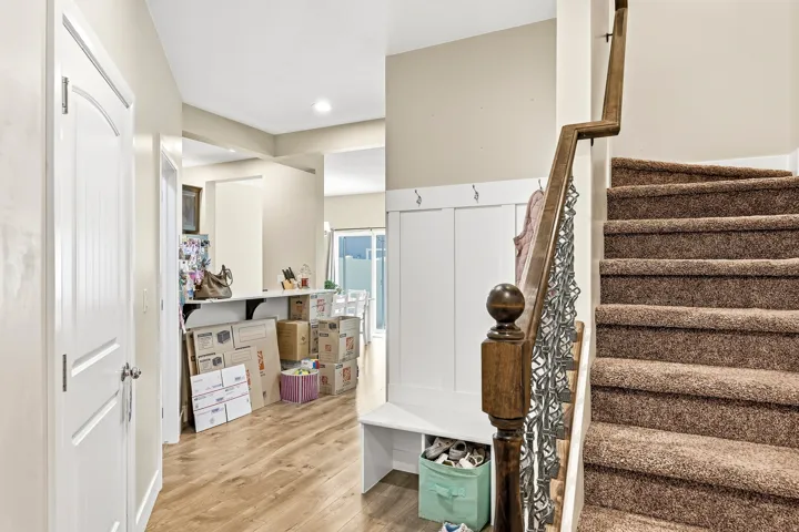 Wood-finish flooring, built-in mudroom bench with coat hooks, carpeted staircase with wrought iron balusters, and wood newel post