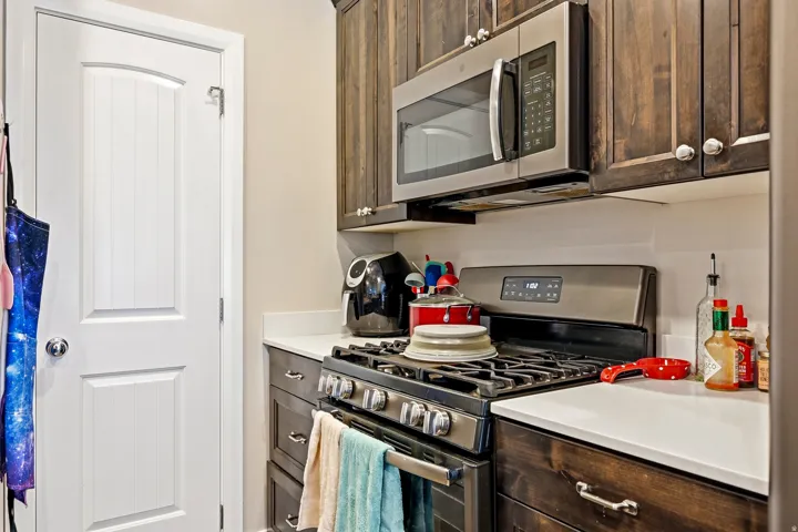 White countertops, rich wood-finish cabinetry, stainless steel microwave, and a gas range