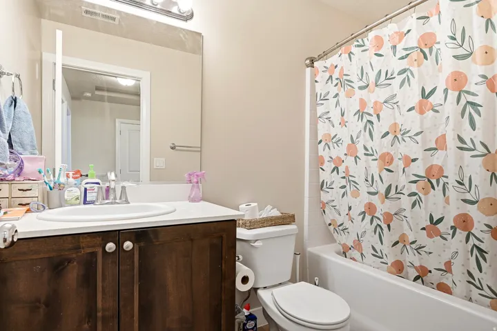 White countertop vanity with wood-finish cabinetry, integrated sink, and wall-mounted mirror