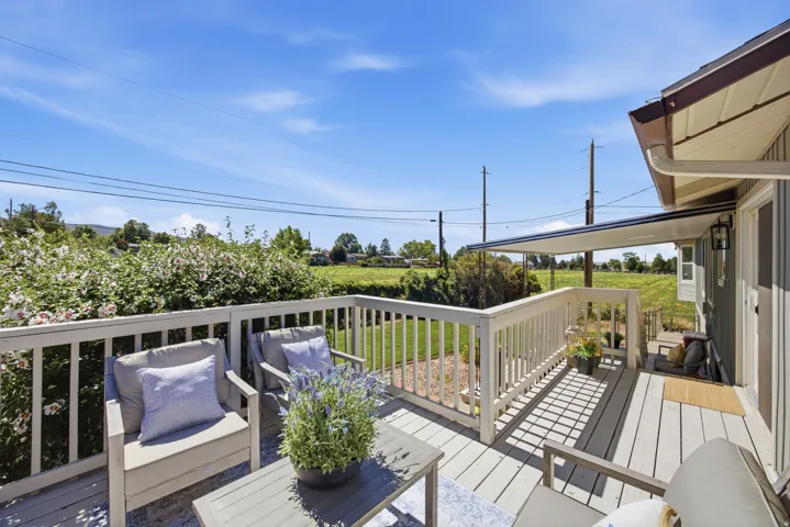 Expansive outdoor deck with white railing, covered patio area, and exterior wall-mounted lighting