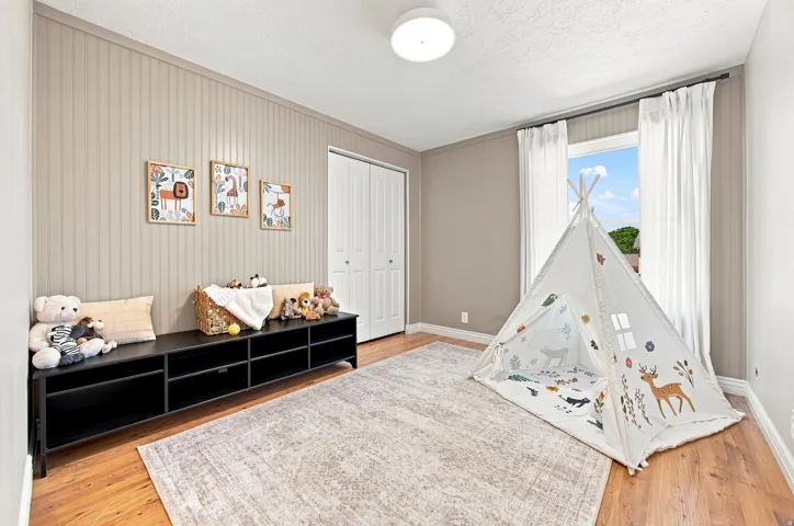 Wood-finish flooring, accent wall with vertical paneling, single window with curtains, and a flush mount ceiling light