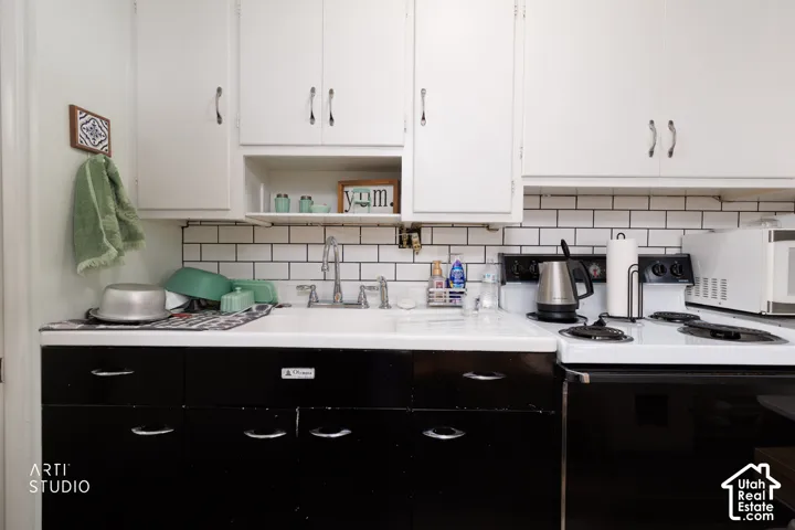 White upper cabinetry with contrasting black lower cabinetry, subway tile backsplash, and a built-in kitchen sink