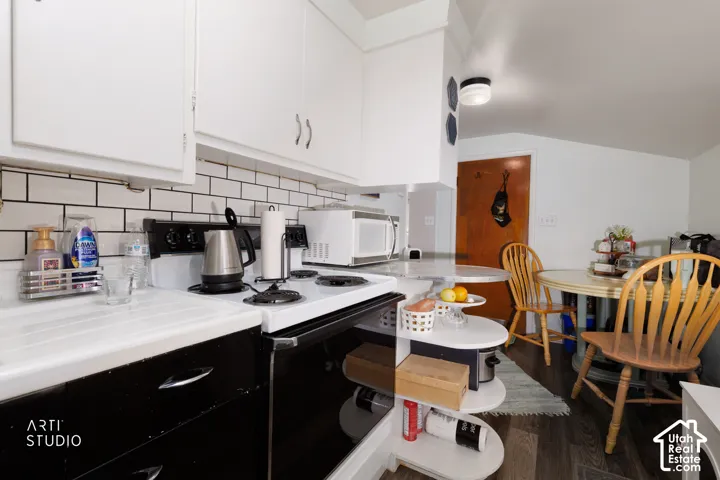 White upper cabinetry with contrasting black lower cabinetry, white subway tile backsplash, white countertop, and wood-finish flooring
