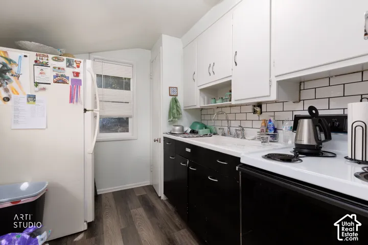 Kitchen featuring wood-finish flooring, white upper cabinetry, black lower cabinetry, a white subway tile backsplash, and a white sink