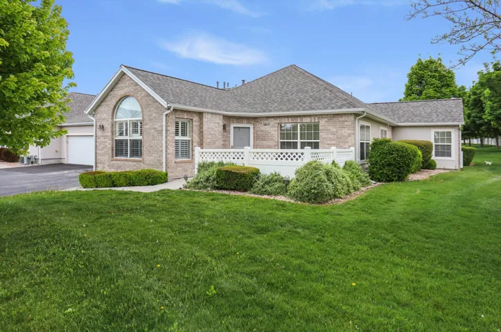Brick exterior with an arched window, white lattice fencing, and an attached garage with a paved driveway