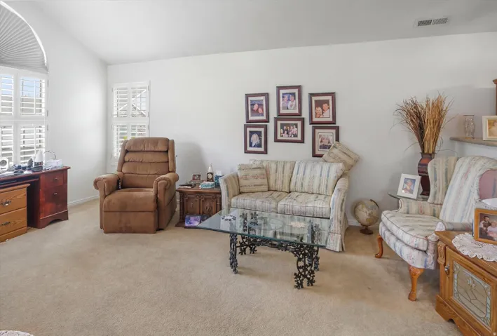 Carpeted flooring, vaulted ceiling, and white plantation shutters