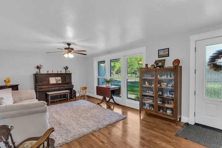 Hardwood flooring, white trim, multiple windows, ceiling fan with integrated lighting, and a white entry door with glass panels
