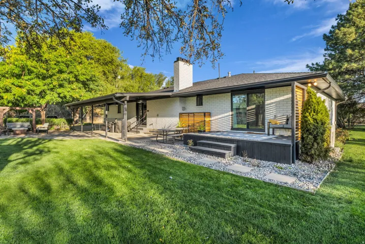 Expansive lawn with mature trees, a covered patio, and a multi-level deck featuring wood-finish privacy screens and sliding glass door access