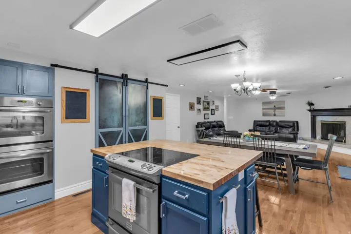 Open-concept kitchen featuring an island with wood-finish countertop, double wall ovens, a built-in cooktop, and barn-style sliding doors
