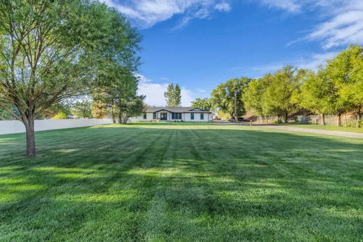 Expansive front lawn with mature trees and a white perimeter fence, featuring a single-story residence with a dark roof and light siding