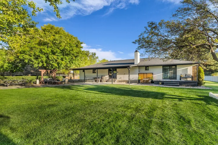 Expansive green lawn, covered patio, outdoor decking, sliding glass doors, and mature trees