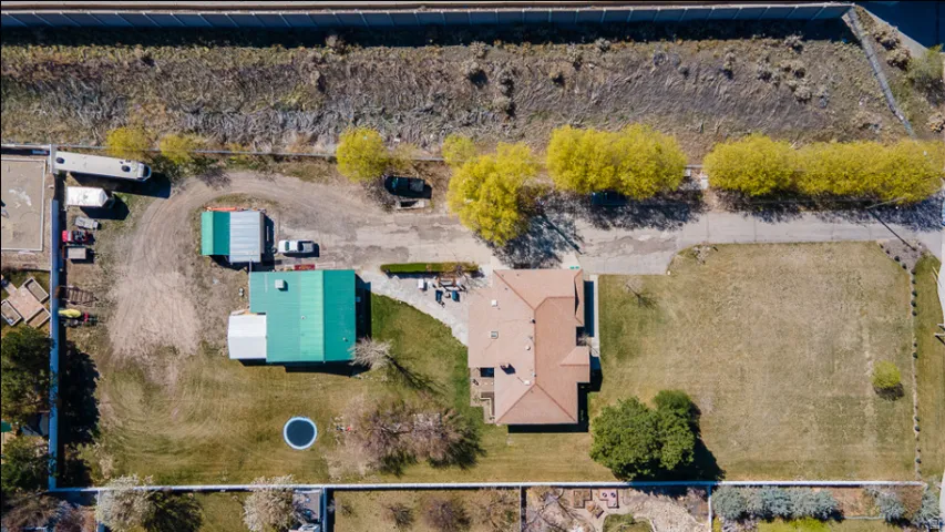 Expansive property featuring two distinct structures, a large undeveloped grassy area, a gravel driveway, and a paved road