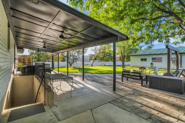 Expansive covered patio with multiple ceiling fans, leading to a brick paver and concrete patio area