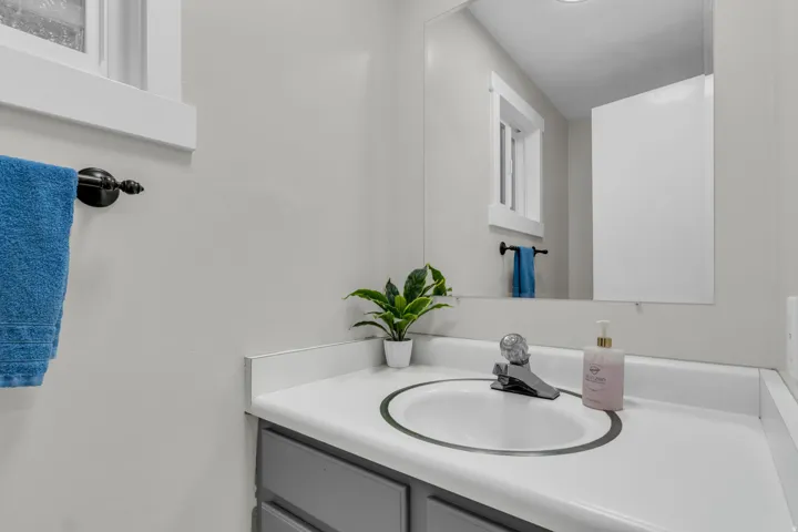 White countertop with an integrated oval sink, chrome faucet, and gray vanity cabinetry