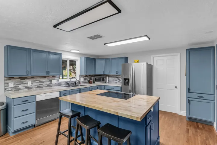 Kitchen featuring blue cabinetry, light countertops, wood-finish flooring, a mosaic tile backsplash, and a central island with a built-in cooktop