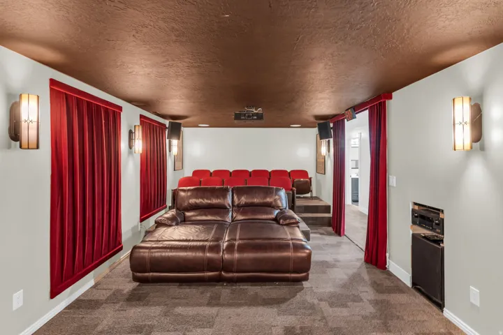 Dedicated media room featuring tiered seating, sconce lighting, red velvet window treatments, and a projector