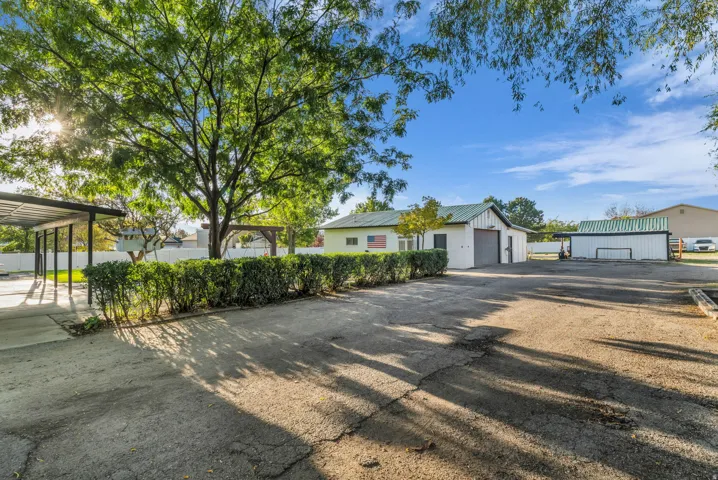 Expansive exterior space with a paved drive, lush mature tree, manicured hedges, and a covered carport