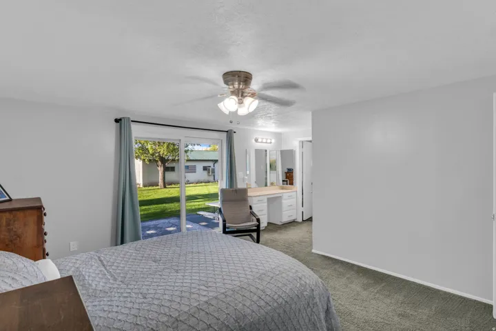Room featuring carpet flooring, ceiling fan with light fixture, sliding glass door with backyard access, built-in vanity with task lighting, and multiple mirrors