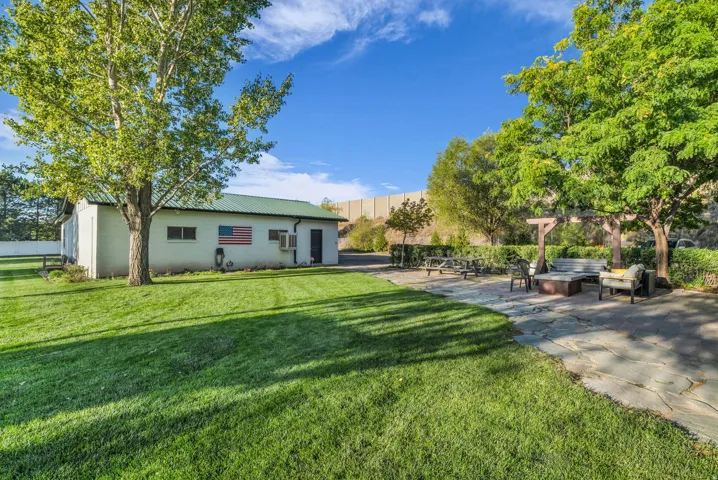 Expansive lawn with mature trees, a stone patio, and a wooden pergola structure