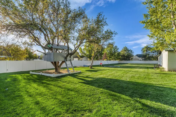 Expansive backyard with a lush lawn, privacy fencing, mature trees, a built-in treehouse, and an exterior storage shed