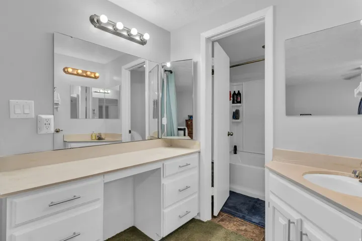 Dual vanity with integrated sink, extensive counter space, white cabinetry, and wall-mounted lighting