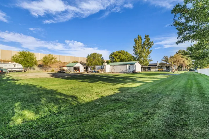 Expansive green lawn, white picket fencing, mature trees, and multiple outbuildings for storage